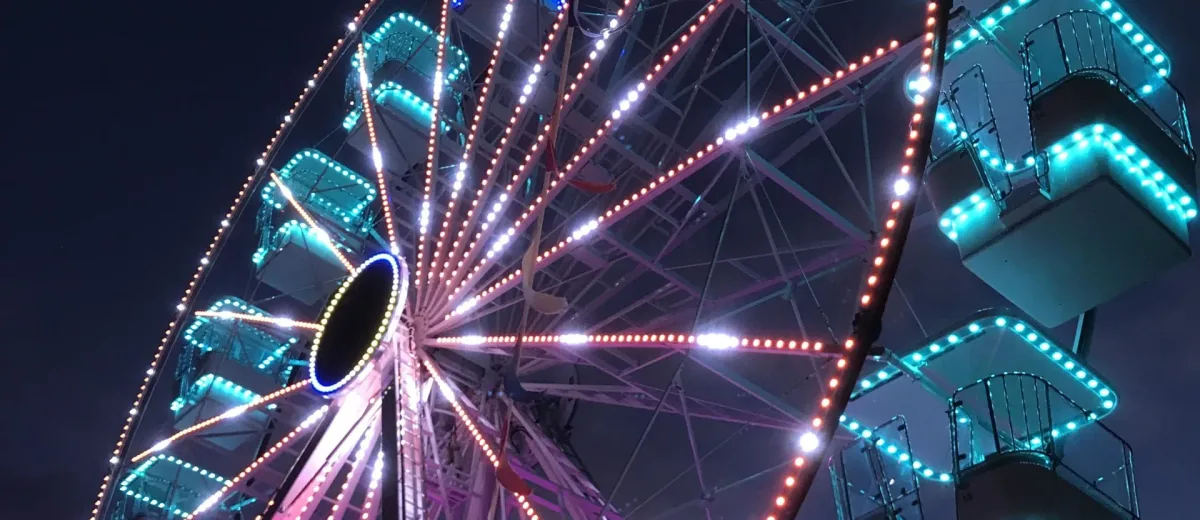 Ferris wheel lit with pink and teal lights at night
